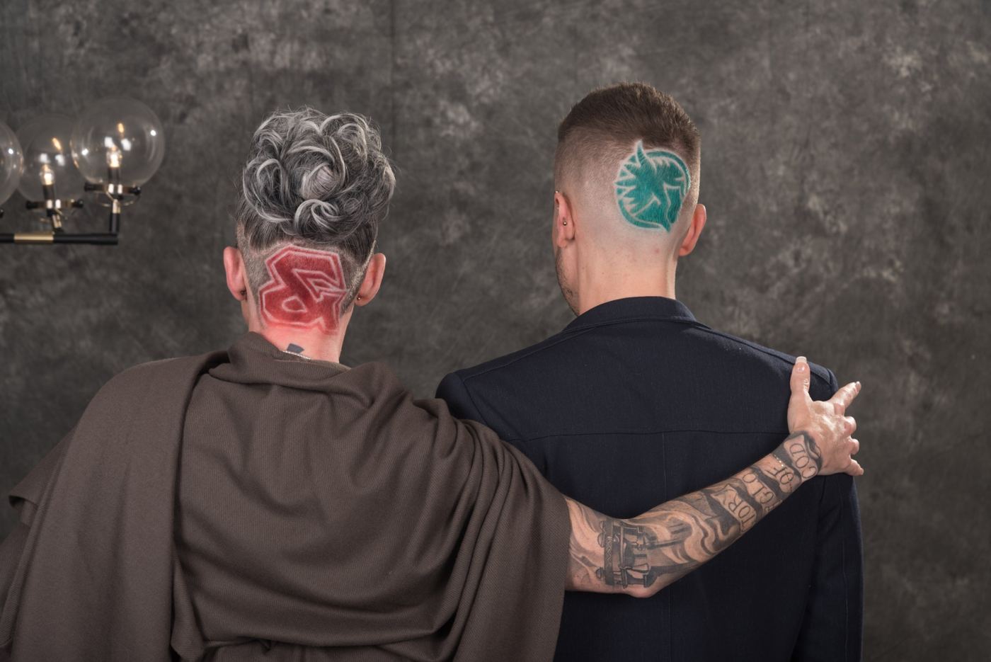 Carrie and Ian from behind, showing their shaved-in designs: a red ampersand and a teal logo