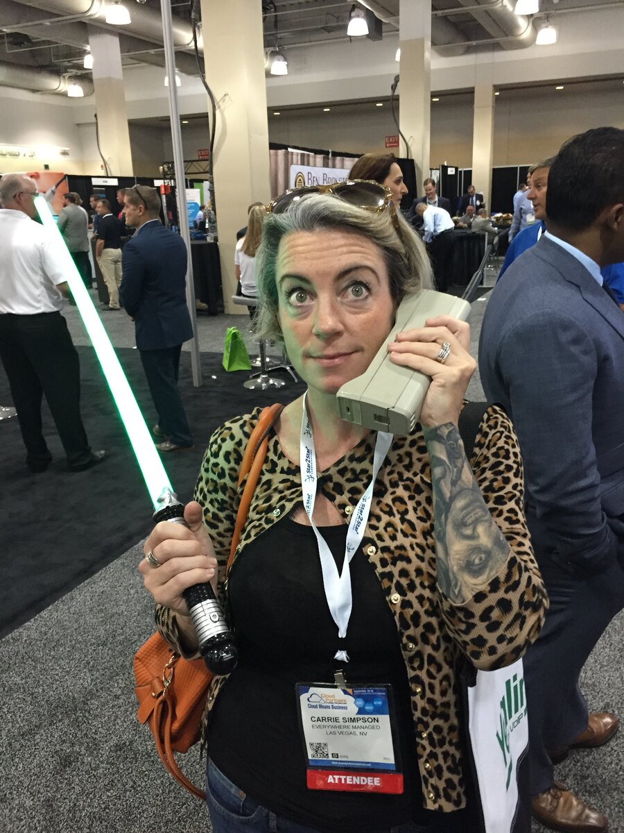 Carrie Simpson holding a phone and a glowing green prop on a conference floor.