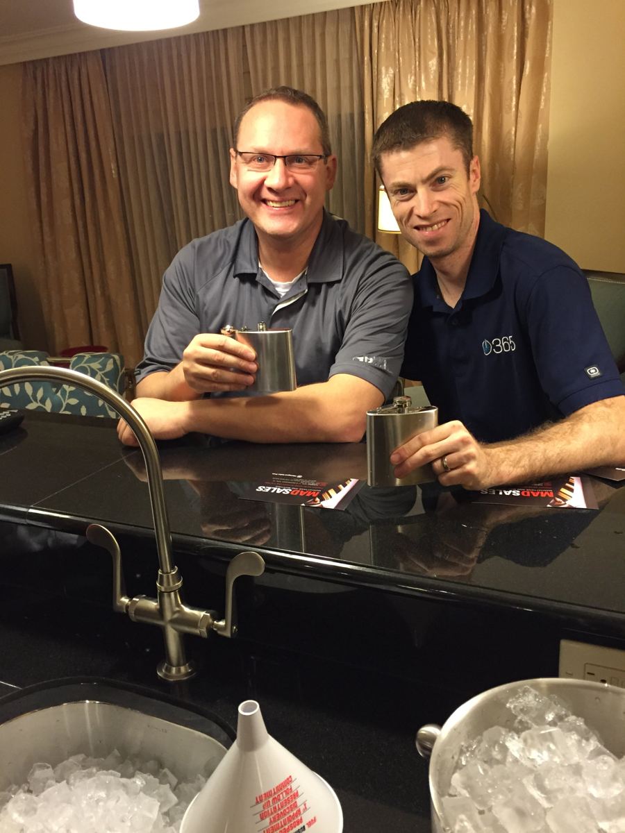 Two friends holding flasks at the suite bar next to buckets of ice
