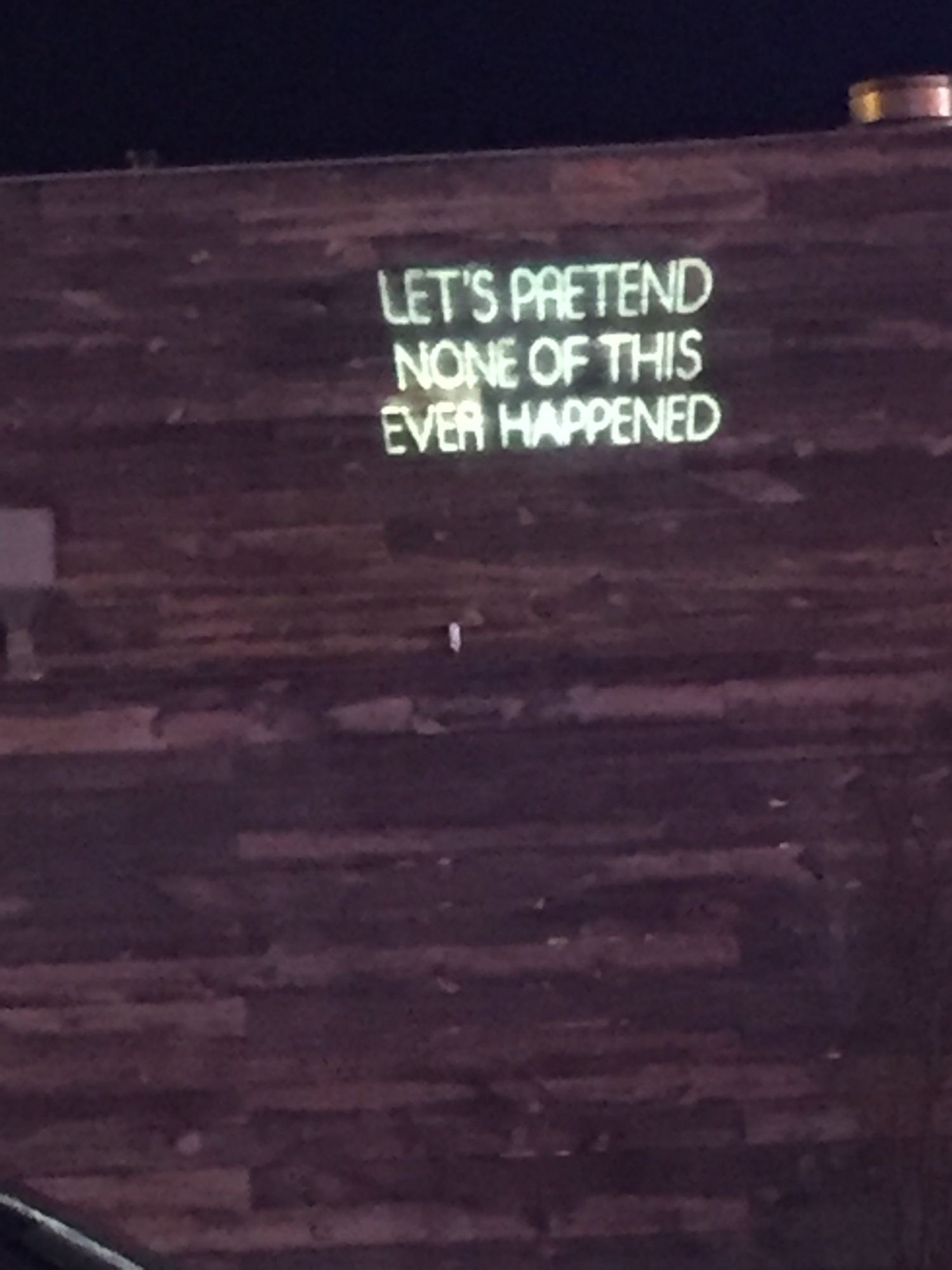 A neon sign on a wood wall that reads: Let's pretend none of this ever happened.