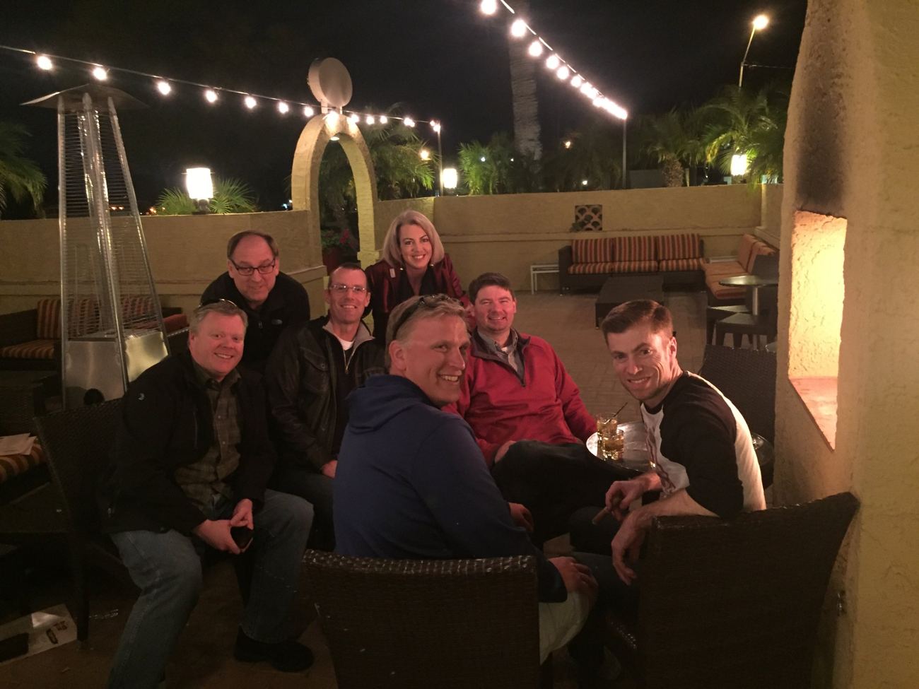 A group of friends with drinks and cigars on a patio under string lights