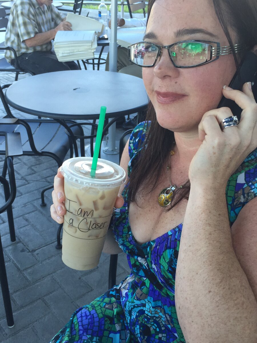 Tracie holding a phone and iced coffee at an outdoor table.
